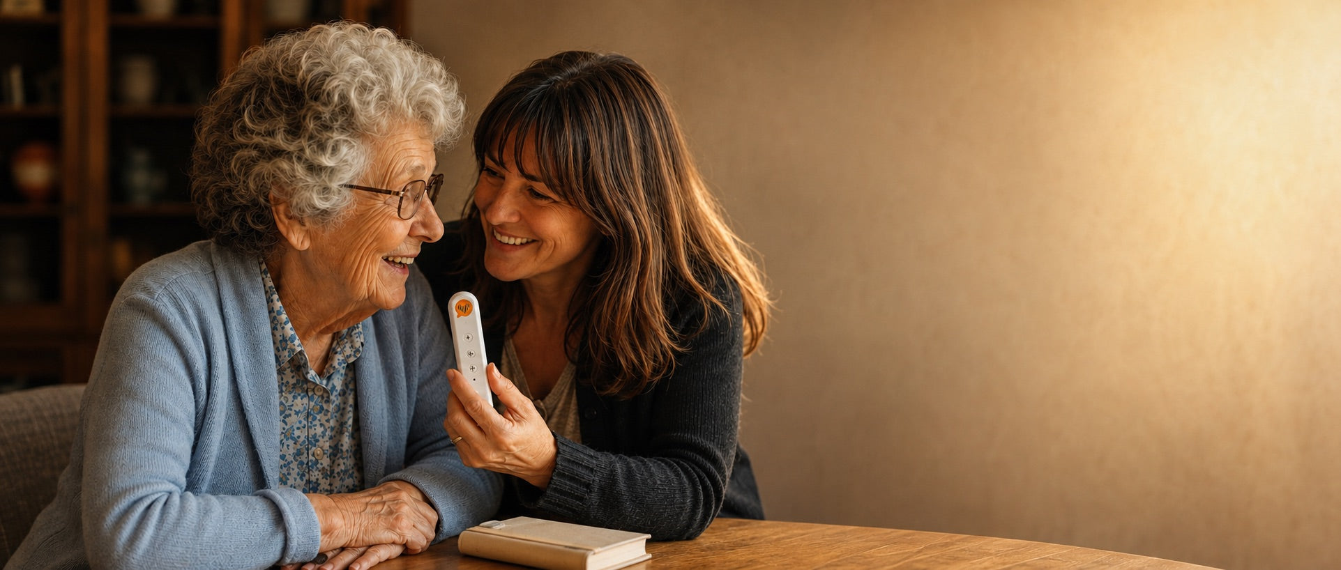 A grandmother speaking into a CoHear recorder at the kitchen table while her daughter listens