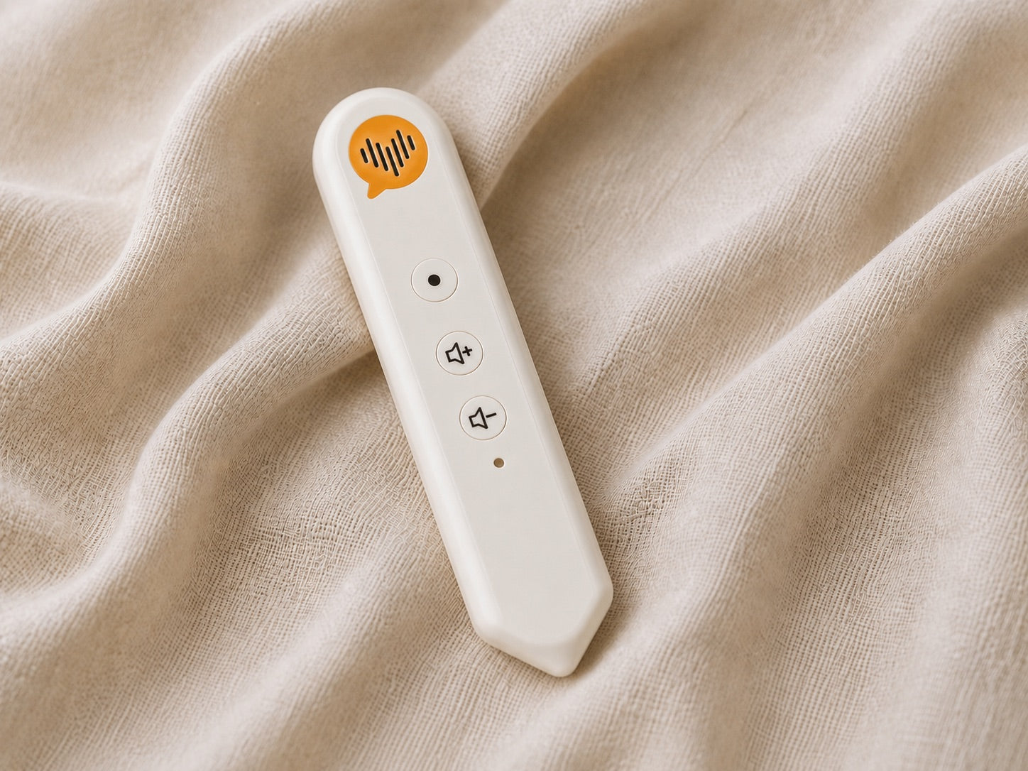 Close-up of the cream CoHear voice recorder with its coral record button and volume controls, resting on soft fabric